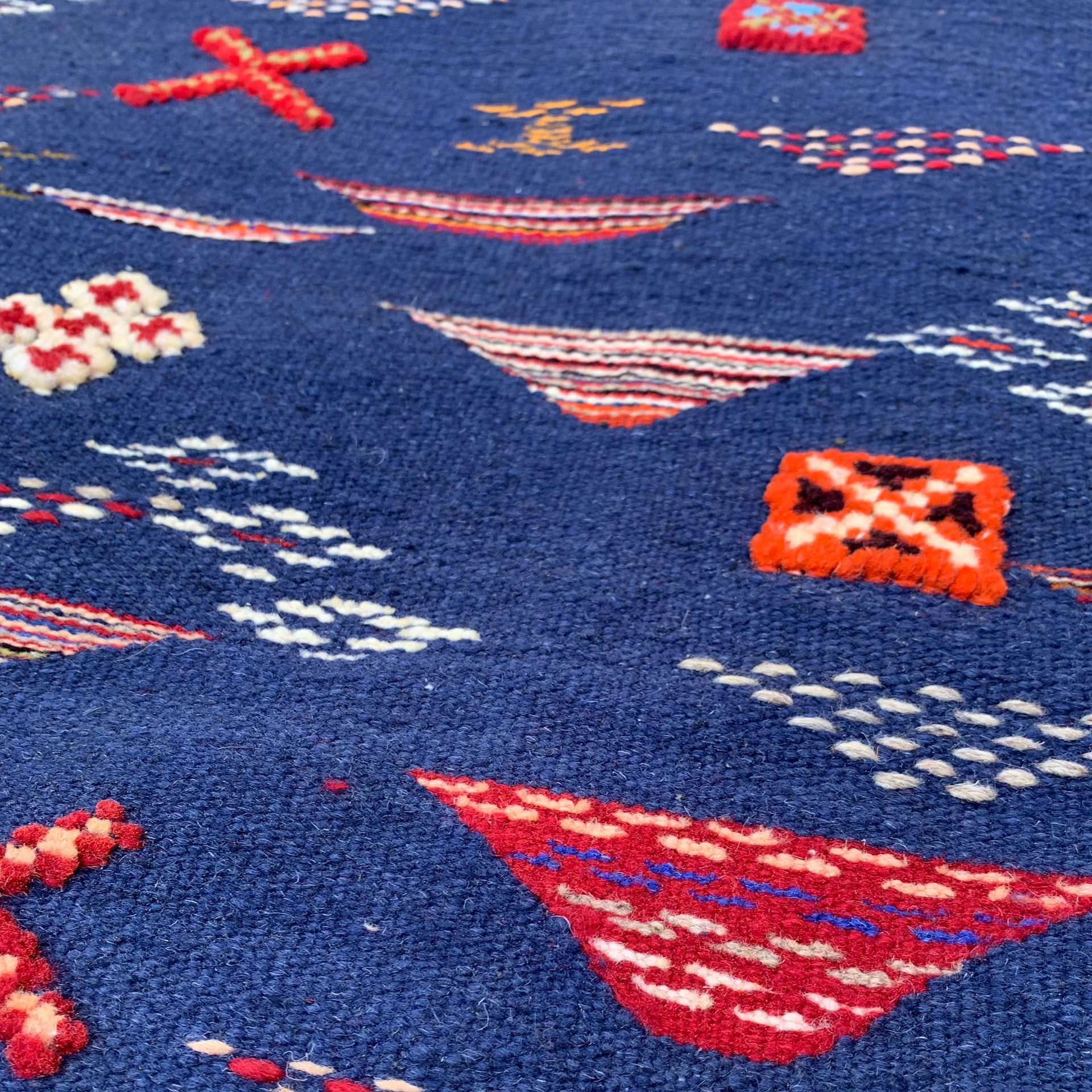 Close-up of a navy blue rug with red and white patterns resembling boats and stars.