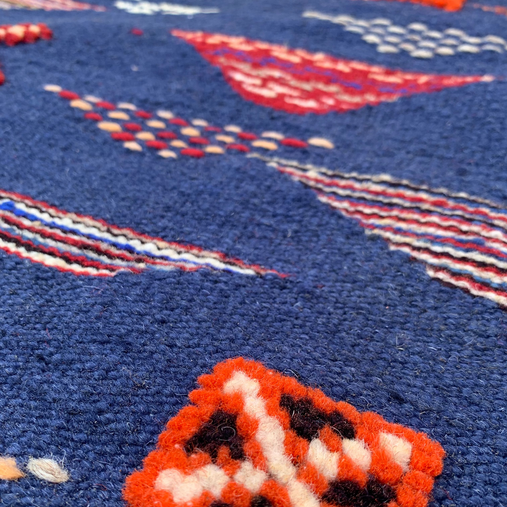 Close-up of a texture navy blue rug with geometric patterns in orange, white, and black on a blue background.
