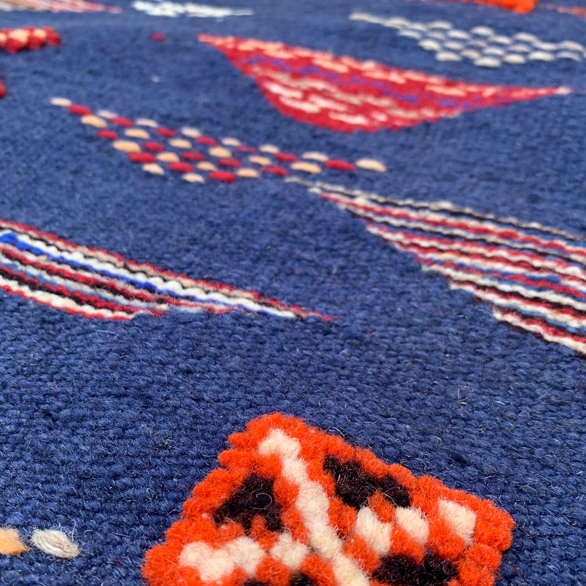 Close-up of a texture navy blue rug with geometric patterns in orange, white, and black on a blue background.