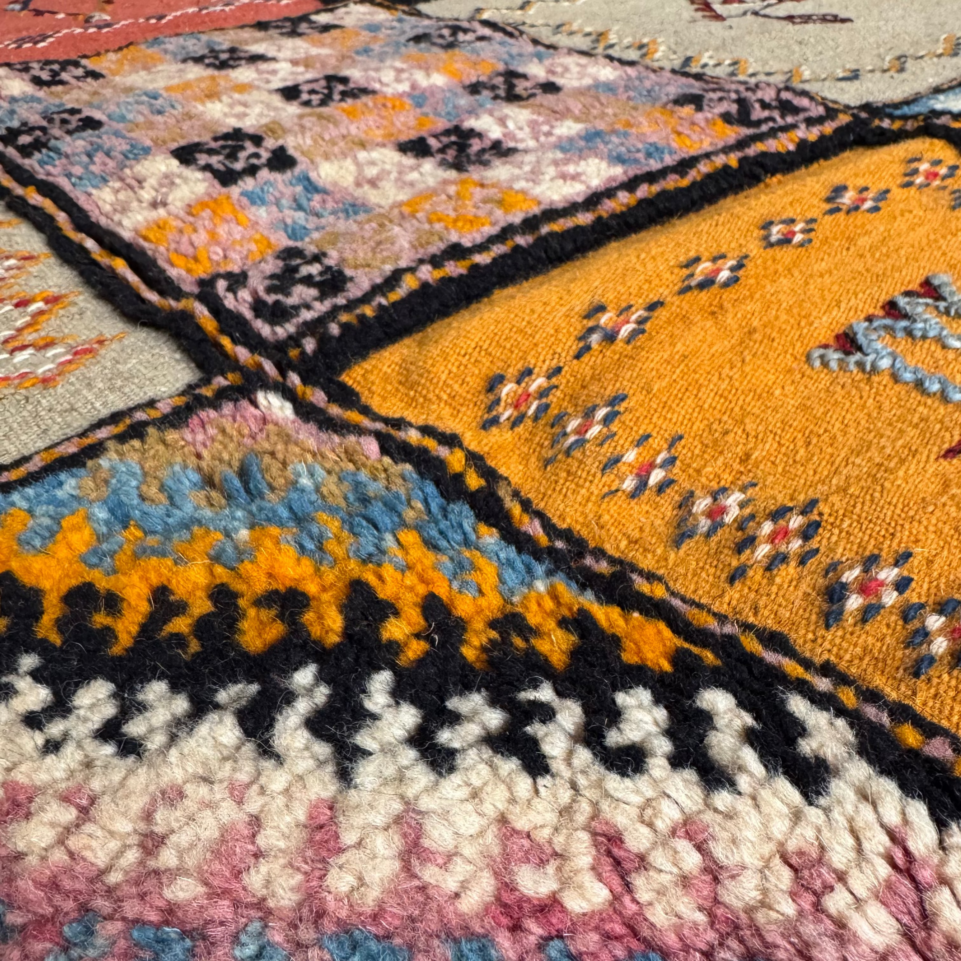 Close-up of handwoven taznakht rug squares with Amazigh symbols, florals, and chevron motifs in natural wool