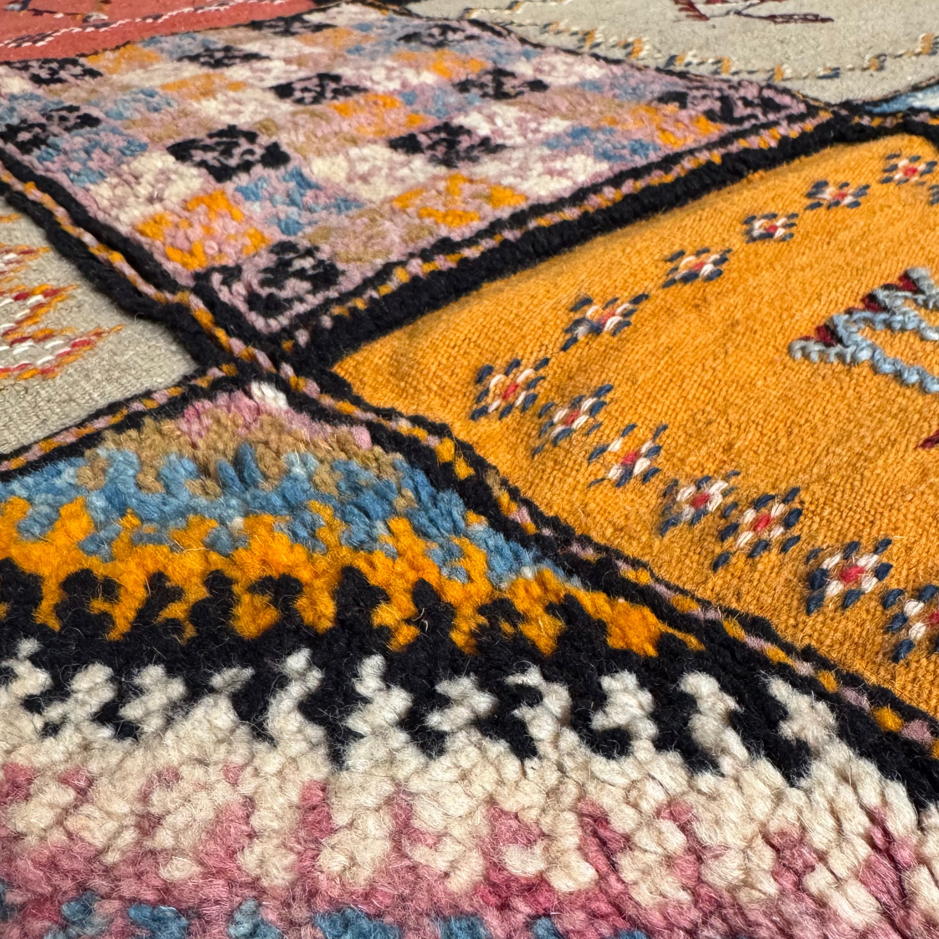 Close-up of handwoven taznakht rug squares with Amazigh symbols, florals, and chevron motifs in natural wool