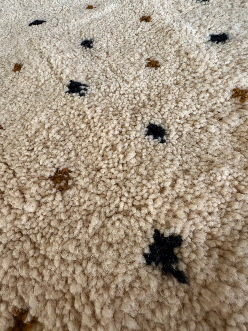 Close-up of ivory wool pile showing small black and brown diamond motifs