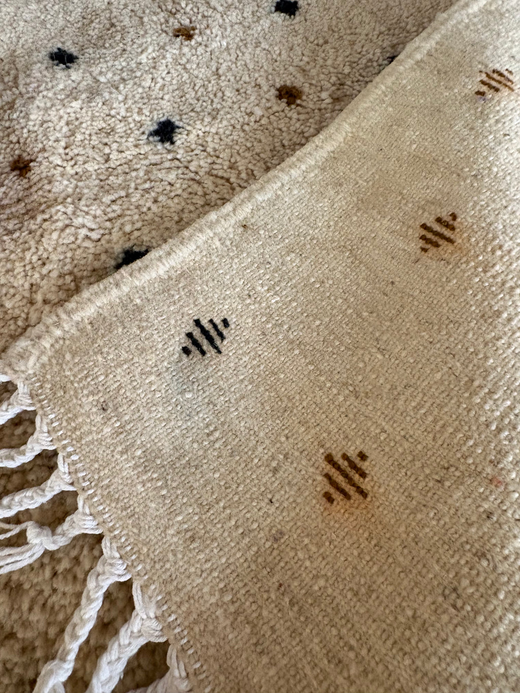 Close-up of ivory wool pile showing small black and brown diamond motifs